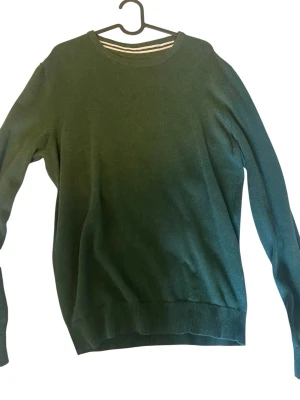 Mörkgrön stickad tröja Pier One - Mörkgrön stickad tröja från Pier One med rund halsringning och ribbade muddar vid ärmslut och nederkant. Enkel och stilren design som passar perfekt till jeans eller chinos. Materialet känns mjukt och bekvämt mot huden.