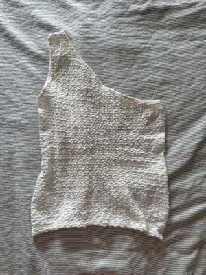 Vit oneshoulder topp från Kappahl - Säljer en vit oneshoulder topp från Kappahl i storlek XS. Den har en stretchigt material så den passar S och skulle även säga M. Perfekt för dig som vill ha en enkel men snygg topp till sommaren.
