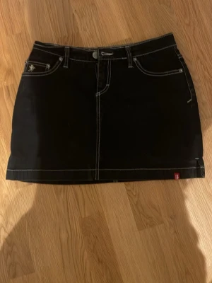Svart kort jeanskjol med kontrastsömmar - Snygg svart jeanskjol med vita kontrastsömmar och klassiska fickor både fram och bak. Köpt på vinted men är i bra skick och säljer pga fel storlek. Skriv för fler frågor