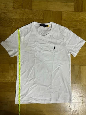 Vit t-shirt från Polo Ralph Lauren - Klassisk vit t-shirt från Polo Ralph Lauren med rund hals och korta ärmar. Tillverkad i mjuk bomull och har den ikoniska broderade loggan i svart på bröstet. Enkel och stilren design som passar till det mesta.