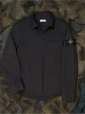 Svart overshirt från Stone Island - Stilren svart overshirt från Stone Island med dragkedja framtill, klassisk krage och bröstficka med lock. Ikonisk logotyp på vänster ärm. Perfekt lager för en modern streetwear-look.