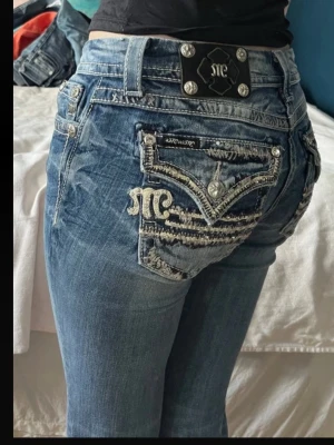 Blå Miss Me jeans med broderade fickor - Säljer ett par blå Miss Me jeans med snygga slitningar och broderade bakfickor med silverdetaljer och knappar. Jeansen har låg midja, raka ben och coola kontrastsömmar. Perfekta för dig som gillar statement-jeans med unik design. Mått : midja 38cm skrev 20cm,  Innerben 77cm , ytterben 98cm, slutet av benen är sömmen upptagen för att passa mig som är 172cm lång bättre, rekommenderar till någon som är 170 och under!
