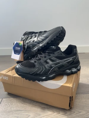 Svarta Asics Gel-Sneakers - Snygga svarta sneakers från Asics med silvriga detaljer och meshpaneler för bra ventilation. Skorna har Ortholite-innersula och GEL-dämpning i sulan för extra komfort. Perfekta för dig som gillar sportig stil och vill ha något bekvämt till vardags.