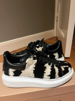 Svarta och vita sneakers med pälslook - Unika sneakers med svart och vit pälsimitation och chunky vit sula. Skorna har svarta skosnören och detaljer i svart läder runt hälen och snörningen. Perfekt för dig som vill sticka ut med ett djurmönstrat och trendigt par sneakers.