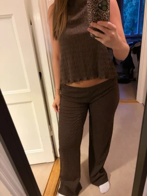 Brunt ribbat loungewear-set - Säljer ett brunt loungewear-set med ribbad struktur. Setet består av ett ärmlöst linne med lös passform och ett par matchande byxor med utsvängda ben. Perfekt för chill dagar hemma eller när du vill vara bekväm men ändå snygg.