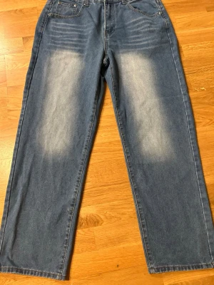 Blå raka jeans med tvättade detaljer - Säljer ett par blå jeans med raka ben och snygga tvättade detaljer på låren. Jeansen har klassisk femficksdesign och normal midja. Materialet är denim i bomull och passformen är avslappnad och trendig.