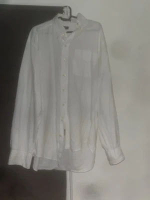 Vit linneskjorta från Gant - Klassisk vit skjorta från Gant i svalt linne. Skjortan har knappar framtill, bröstficka och button-down krage. Perfekt för en clean och stilren look. Långärmad modell med avslappnad passform.