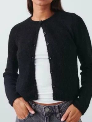 Svart cardigan - En svart, enkel kofta med rund halsringning och knäppning framtill. Koftan har lång ärm och är gjord i ett mjukt, stickat material. Perfekt att slänga över en t-shirt eller linne för en chill look.