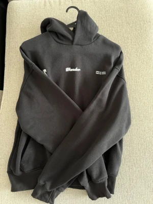 Svart hoodie med tryck Bershka - Säljer en svart hoodie med huva och magficka. På bröstet står det 'Wander' i vitt samt texten 'Wild or urban, free by choice.' och en liten grafisk detalj. Hoodien har ribbade muddar och är i mjukt bomullsmaterial.