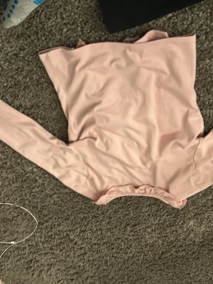 Ljusrosa omlottkofta med volang - Supersöt ljusrosa omlottkofta med volangkant längs öppningen och knytband i midjan. Koftan har långa ärmar och är gjord i ett mjukt, stretchigt material som känns skönt mot huden. Perfekt för att addera en romantisk touch till din outfit.
