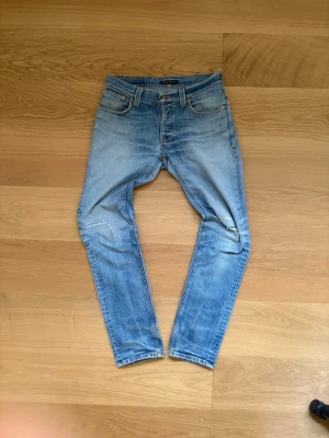 Nudie Jeans - Grim Tim W29 L32 Ljusblå - Riktigt snygga Nudie Jeans med en fet tvätt. | W29 | L32. | Riktigt fint skick, finns några fabriksgjorda slitningar samt en lagning vid höger knä. | Längd: 104cm, Midja: 40 cm | Pris ej hugget i sten, skriv vid minsta fundering.