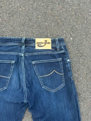 Mörkblå jeans från Jacob Cohen - Snygga mörkblå jeans från Jacob Cohen med raka ben och klassiska bakfickor med kontrastsömmar. Jeansen har en patch med logga bak i midjan och är tillverkade i ett mjukt denimtyg. Perfekta för en avslappnad men stilren look.