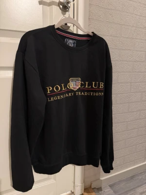 Svart sweatshirt Vinson Polo Club - Svart sweatshirt från Vinson Polo Club med gul text och broderad logga på bröstet. Klassisk rund halsringning och långa ärmar. Tröjan har en avslappnad passform och ribbade muddar vid ärmslut och nederkant. Perfekt för en sportig och stilren look.