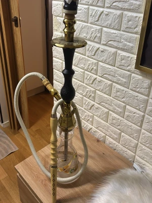 Klassisk vattenpipa i guld och svart från Saudi arabien - Säljer en stilren vattenpipa med detaljer i guld och svart. Basen är genomskinlig glas med guldfärgade mönster och slangen är vit med gulddetaljer. Perfekt för dig som vill ha en snygg och funktionell shisha till samlingen.