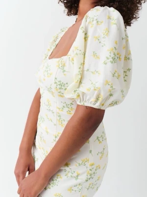 Vit blommig klänning med puffärm - Söt vit klänning med gult och grönt blommönster, puffiga kortärmar och fyrkantig ringning. Klänningen har en slits framtill och figurnära passform, perfekt för sommarens alla tillfällen.