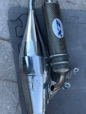 ZX avgassystem till moped - Säljer ett ZX avgassystem till moped med kolfiber-look på ljuddämparen och blankt metallrör. Passar dig som vill ha sportigt ljud och snygg stil på mopeden. Märkt med ZX-logga och har robust konstruktion. Passar till piaggio nrg power