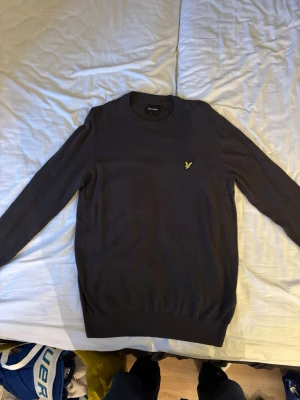 Mörkgrå stickad tröja Lyle & Scott - Snygg mörkgrå stickad tröja från Lyle & Scott med rund halsringning och den klassiska gula logon broderad på bröstet. 