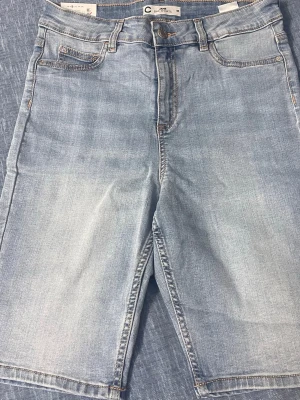 Ljusblå jeansshorts med fem fickor - Säljer ett par ljusblå jeansshorts i klassisk modell med fem fickor och knappgylf. Shortsen har en rak passform och är tillverkade i mjuk denim som passar perfekt till sommaren.