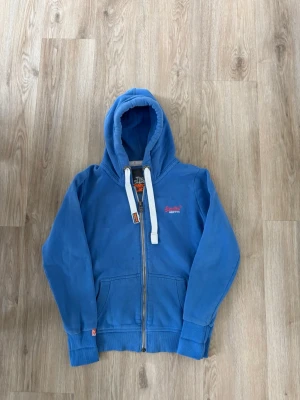 Superdry zip hoodie - Säljer denna Superdry zip hoodie i mycket bra skick. Storlek L men sitter mer som S/M. Passar perfekt för dig som är mellan 165-172! Hör av er vid frågor eller minsta fundering 🙌OBS! Finns några små fläckar men som troligen går bort i tvätt!   Längd: 60 cm  Bred: 45,5 cm  Ärm: 62 cm