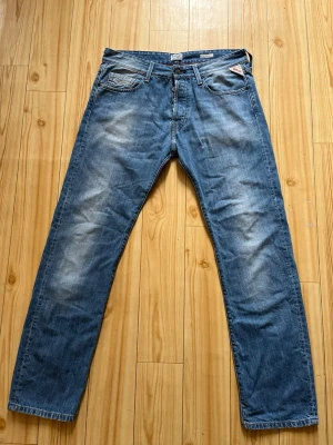 Blå raka jeans från Replay - Säljer ett par blå jeans från Replay i modellen JENNON. Jeansen har raka ben, klassisk femficksdesign och snygga slitningar framtill. Tillverkade i denim med Replay-logga på myntfickan. Perfekta för en avslappnad och trendig look.