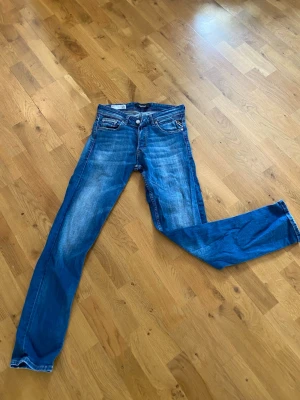 Replay jeans slitningar och tvätt  - Säljer ett par blå replay jeans med raka ben och snygga slitningar framtill och baktill. Jeansen har klassiska fem fickor och coola detaljer på bakfickorna. Materialet är denim i bomull och passformen är avslappnad men ändå stilren.