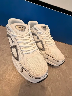 H&M Vita Skor - Snygga vita H&M sneakers med mesh och läderdetaljer. Skorna har svarta och grå inslag på sidorna och en chunky sula för modern look. Klassisk snörning och tydlig H&M-logga på plösen. Perfekta för dig som gillar exklusiva och trendiga sneakers.