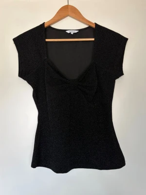 Glittrig topp - Glittrig topp med rosettdetalj. Använd några få gånger.