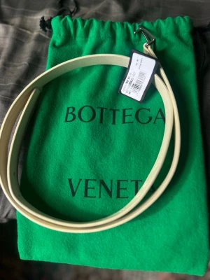  Bottega Veneta belte - Snyggt och stilrent ljust bälte från Bottega Veneta i calf läder. Bältet har en minimalistisk metallspänne och kommer med en grön dustbag med logga. Perfekt accessoar för att lyfta din outfit.