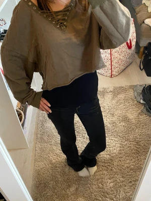 Croppad topp med snörning - Säljer en croppad brun grön topp med snörning i halsen och oversized passform. Toppen har långa ärmar och en avslappnad look, perfekt för dig som gillar streetstyle. Materialet känns mjukt och bekvämt.