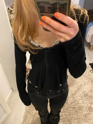 Svart långärmad topp med spets Gina Tricot - Säljer en svart långärmad topp från Gina Tricot med v-ringning och vit spetskant. Toppen har en liten rosett framtill och är figurnära med en feminin touch. Perfekt att styla med jeans eller kjol.