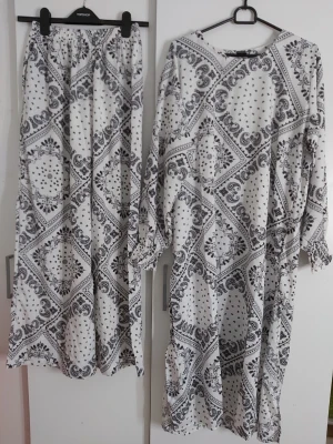 Vit och svart långärmad blus med mönster och vidben byxor - Säljer en vit långärmad blus med svart paisley- och prickmönster och vidben byxor. Blusen har lös passform och är tillverkad i ett lätt, mjukt tyg som känns skönt mot huden. Perfekt för dig som gillar boho-vibbar och vill ha något unikt i garderoben.