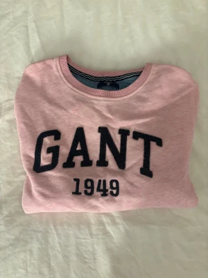 Rosa sweatshirt från GANT - Säljer en ljusrosa sweatshirt från GANT med svart broderad logga och årtalet 1949 på bröstet. Tröjan har rund halsringning, långa ärmar och ribbade muddar vid ärmslut och nederkant. Perfekt för en avslappnad och stilren look. Tröjan är i storlek 158/164💕