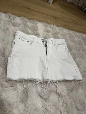 Vit jeanskjol från g perfect jeans - Säljer en vit jeanskjol från gina. Kjolen är kort med rå kant nertill och har klassiska jeansdetaljer som fickor fram och bak, samt dragkedja och knapp i midjan. Perfekt för dig som gillar en enkel ren stil.