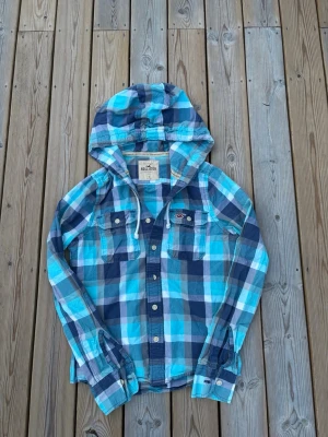 Hollistee skjorta med huva ~ Vintage  - Säljer denna Hollister skjorta med huva i mycket bra skick och som är Vintage så därmed väldigt eftertraktad. Storlek S. Passar perfekt för dig som är mellan 165-173! Hör av er vid frågor eller minsta fundering 🙌  Längd: 64 cm  Bred: 45,5 cm  Ärm: 68 cm