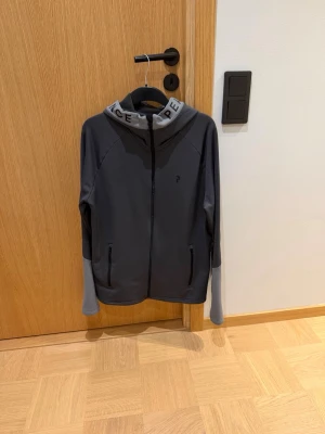 Mörkgrå zip hoodie Peak Preformance - Stilren zip hoodie från Peak Preformance. Skick 8/10. Väldigt sparsamt använd. Skön och passar till det mesta.