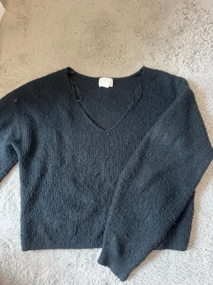 Svart stickad tröja från H&M - Mysig svart stickad tröja från H&M med v-ringning och långa ärmar. Tröjan har en enkel och stilren design som passar perfekt till många olika outfits. Materialet är mjukt och bekvämt, perfekt för kyligare dagar.