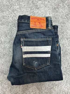 Momotaro Jeans striped - Säljer ett par mörkblå jeans från Momotaro med raka ben och två vita signaturränder på bakfickan. Jeansen är i ganska bra skick med fina fades.