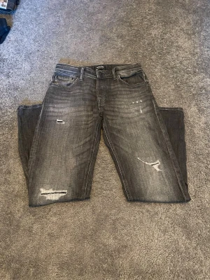 Grå slitna jeans med raka ben - Säljer ett par grå jeans med slitningar och hål på benen. Jeansen har fem fickor, normal midja och raka ben. Hör av er vid frågor eller funderingar 
