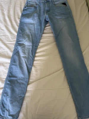 Ljusblå raka jeans herr - Säljer ett par ljusblå jeans från Replay med rak passform och klassisk femficksdesign. Jeansen har normal midja och bälteshällor. Materialet är denim i bomull och färgen är en snygg tvättad ljusblå ton. Perfekta till en avslappnad stil. Model Anbass hyperflex
