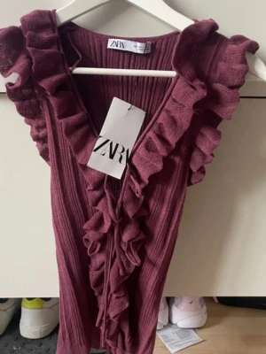 Vinröd ribbad topp med volanger Zara - Supersnygg vinröd ribbad topp från Zara med volangdetaljer längs ärmhålen och v-ringning. !Aldig använd och lappen kvar!