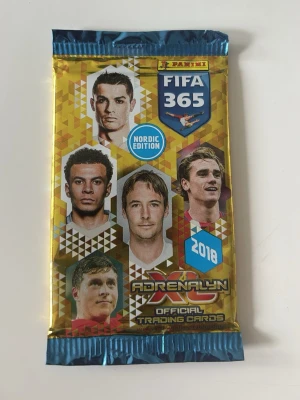 Panini FIFA 365 Adrenalyn 2018 paket - Oöppnat samlarpaket med officiella Panini FIFA 365 Adrenalyn XL trading cards, Nordic Edition från 2018. Förpackningen är guldfärgad med blå detaljer och har bilder på kända fotbollsspelare på framsidan. Perfekt för samlare av fotbollskort.