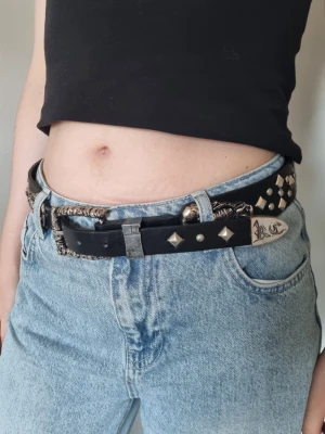 Bälte I fusk läder med dekorationer och spikes  - Fuskande bälte med metall dekorationer och spokikes, studs, skorpioner. 95cm