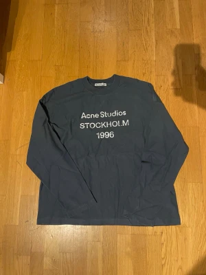  Acne Studios sleeve - Säljer en blå långärmad t-shirt från Acne Studios med trycket 'Acne Studios STOCKHOLM 1996' på bröstet. Klassisk rund hals och relaxed fit. Perfekt för dig som gillar stilrena och tidlösa plagg med en touch av streetwear.