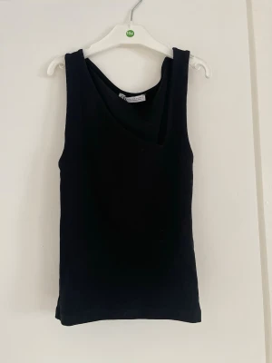 Svart linne/topp - Snygg svart linnetopp med asymmetrisk halsringning. Toppen är ärmlös och har en enkel, stilren design som går att styla på många sätt!!