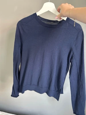 Mörkblå finstickad tröja - En enkel och stilren mörkblå tunn stickad tröja med rund halsringning och långa ärmar. Tröjan har en mjuk känsla och ribbade muddar vid ärmslut och nederkant. Perfekt att matcha med jeans eller kjol. Har ett pyttelitet hål vid ena armen. Den har också en slits på högra sidan. Den är i kashmir. Org pris 800