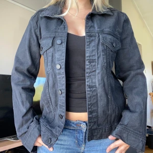 Svart jeansjacka med knappar ginatricot  - Säljer en svart jeansjacka från ginatricot med klassisk krage och knäppning framtill. Jackan har två bröstfickor med lock och knappar samt sömdetaljer längs fram- och baksidan. Är storlek M men skulle säga den är liten i storleken då jag vanligtvis har S 