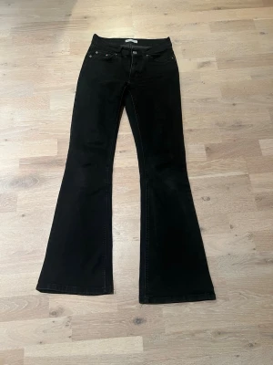 Svarta bootcut jeans från Gina Tricot, stl 34 - Snygga svarta bootcut jeans från Gina Tricot, med klassisk femficksdesign och utsvängda ben. Jeansen har normal midja och är tillverkade i ett mjukt denimtyg som sitter skönt. Perfekta för dig som gillar en trendig siluett.