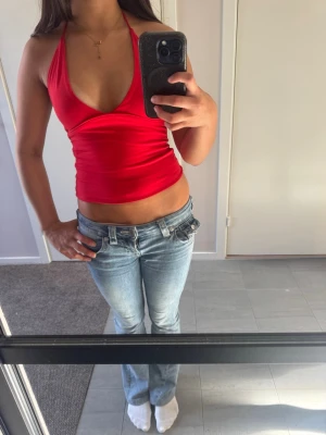 Röd halterneck topp - Snygg röd halterneck topp med djup urringning och smala band som knyts i nacken. Toppen är figurnära och croppad, perfekt till jeans eller kjol. Tillverkad i mjukt stretchigt material som sitter skönt mot kroppen.
