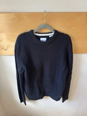 Mörkblå stickad tröja från Jack & Jones - Säljer en snygg mörkblå stickad tröja från Jack & Jones. Tröjan har en klassisk rund halsringning och är perfekt för alla tillfällen. Den är i storlek S och har en stilren design som passar till det mesta. Perfekt för dig som gillar en enkel och stilren look. Helt ny!