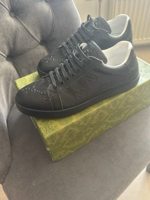 Svarta fin sneakers mönster - Snygga svarta sneakers  med präglat mönster på sidan och ovandelen. Skorna har svarta skosnören, vit insida och guldfärgad med logga på hälen. Tillverkade i en mix av läder och textil för en exklusiv känsla.